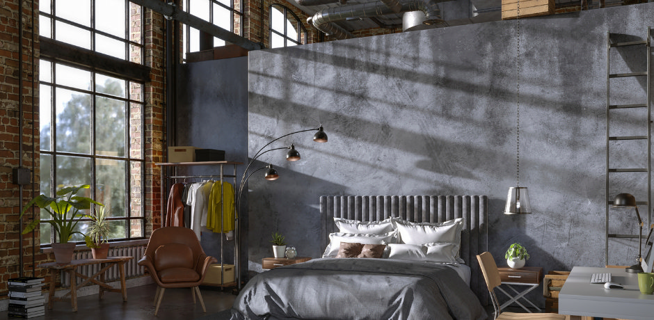 Loft‑style industrial bedroom featuring exposed brick and concrete walls, steel factory windows, and a grey upholstered bed with layered neutral linens.