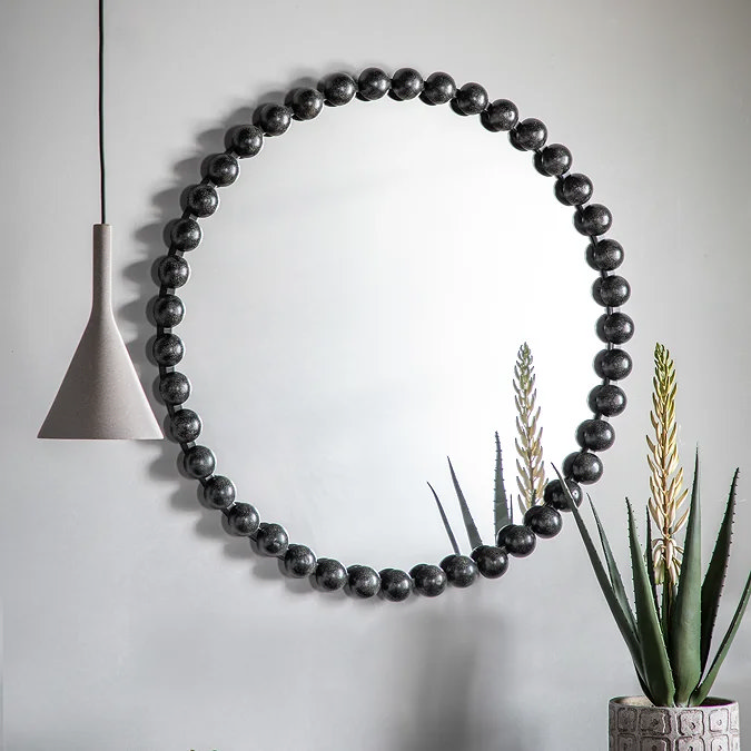 Round black wall mirror with oversized beaded edge frame, creating a bold modern statement in a living room.