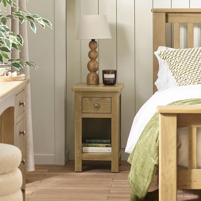bedroom with small oak bedside table with drawer and open shelf beside wooden bed