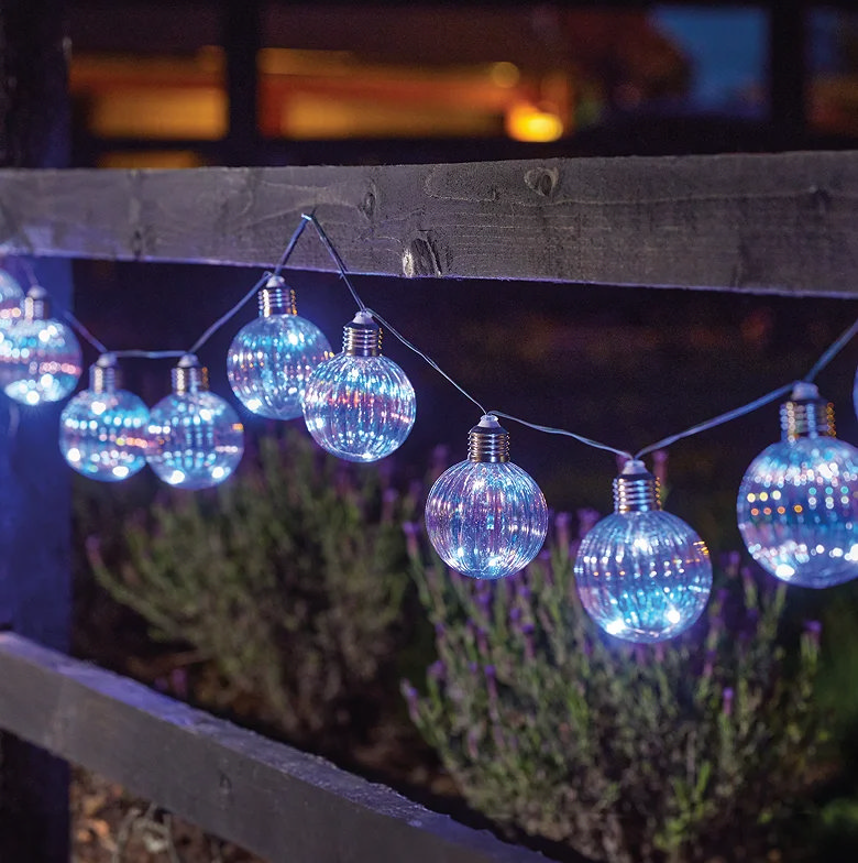 Firefly orb string lights hanging along a garden fence at night