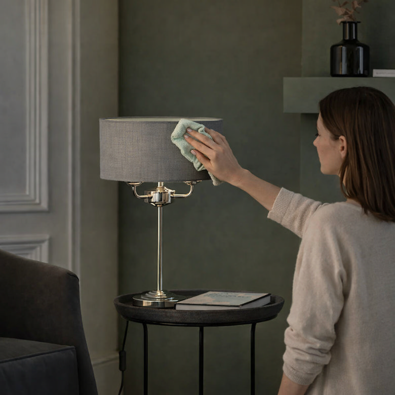Woman wiping a table lamp and lampshade during living room spring cleaning