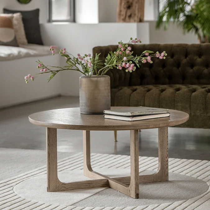 Round wooden coffee table styled with a vase of flowers and stacked books in a calm Scandi living room
