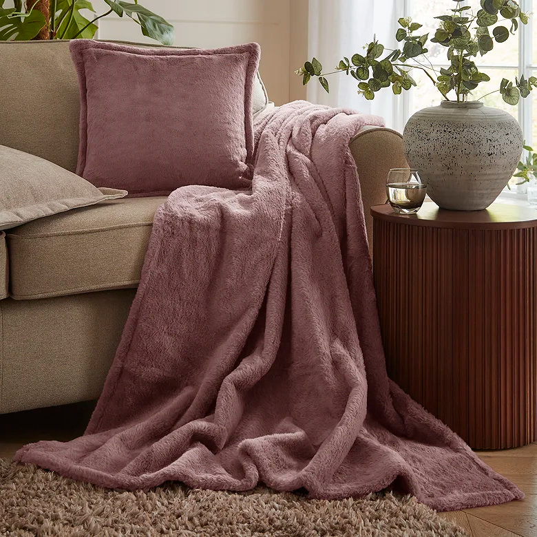 Soft pink throw blanket and cushion styled on sofa with side table and vase
