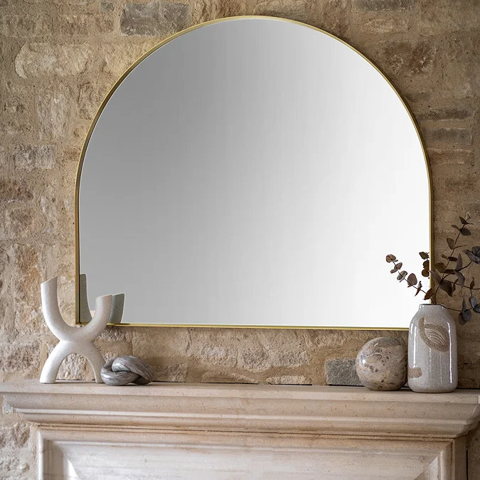 Elegant arched wall mirror with slim gold frame styled above a stone fireplace, adding light and height to a modern living room.