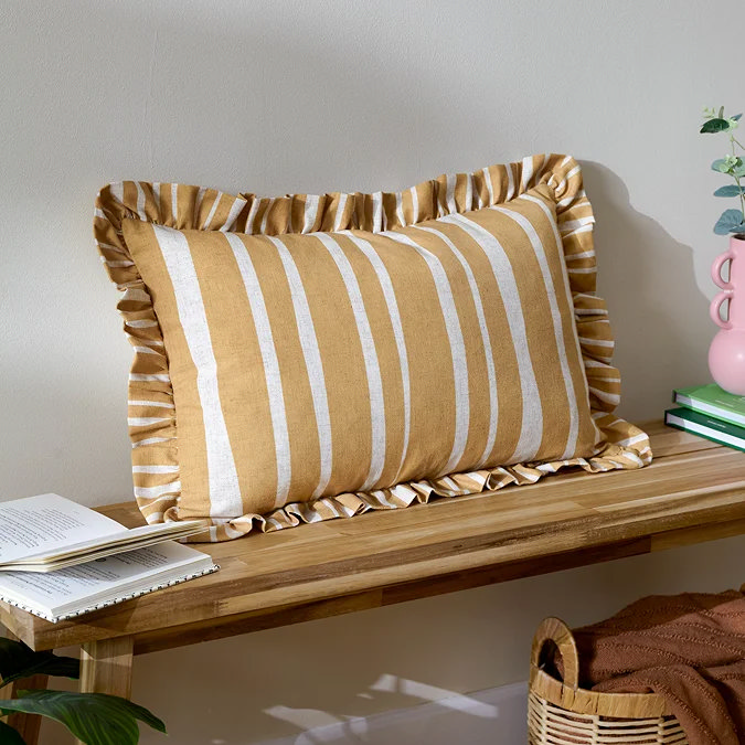Butter yellow striped cushion with ruffled edge on wooden bench.