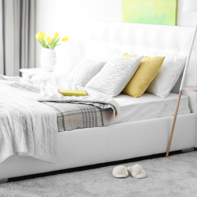 Bright bedroom with layered blankets, knitted cushions and soft slippers creating a warm, cosy feel