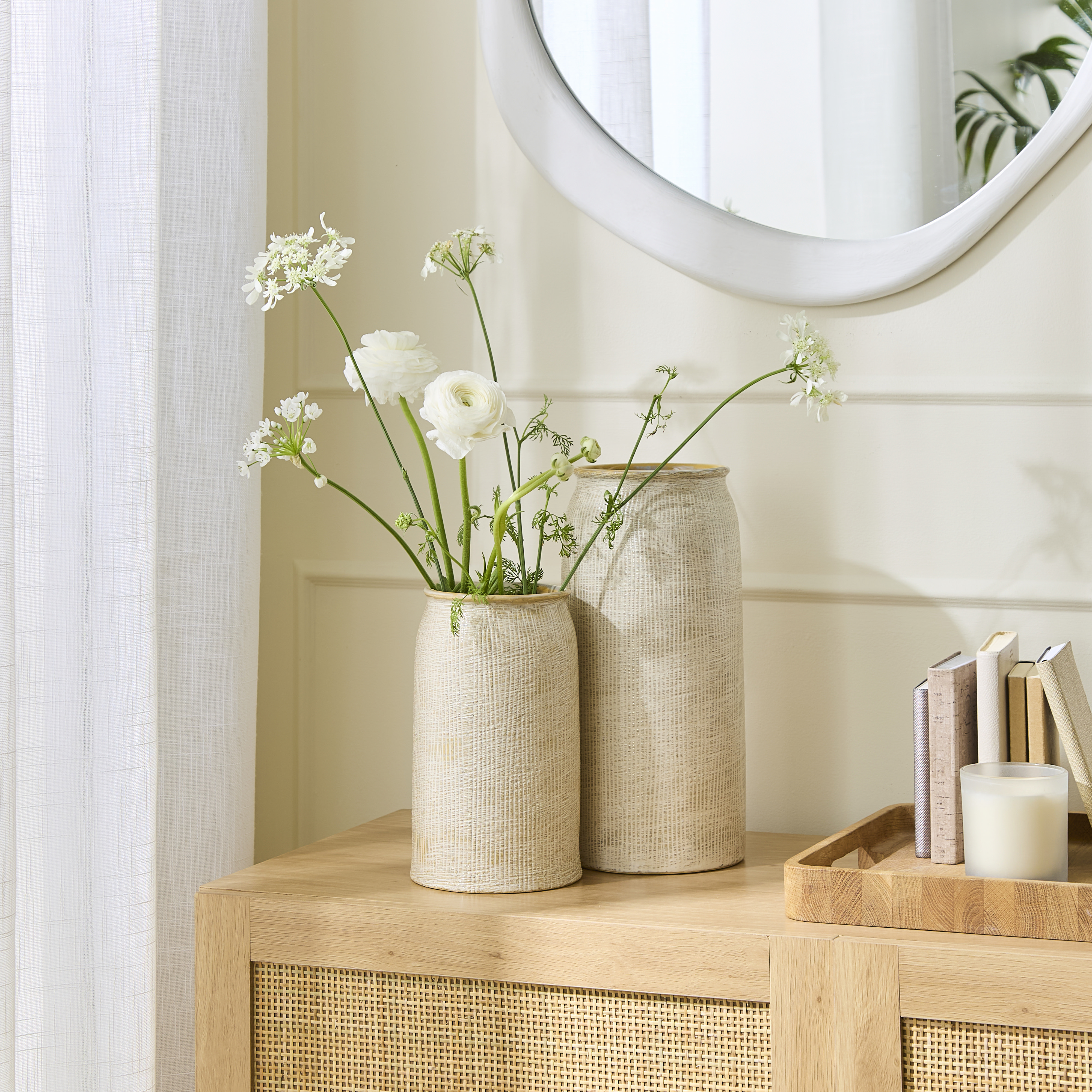 Wooden tray with small books and candle styled on cabinet beside vases of flowers