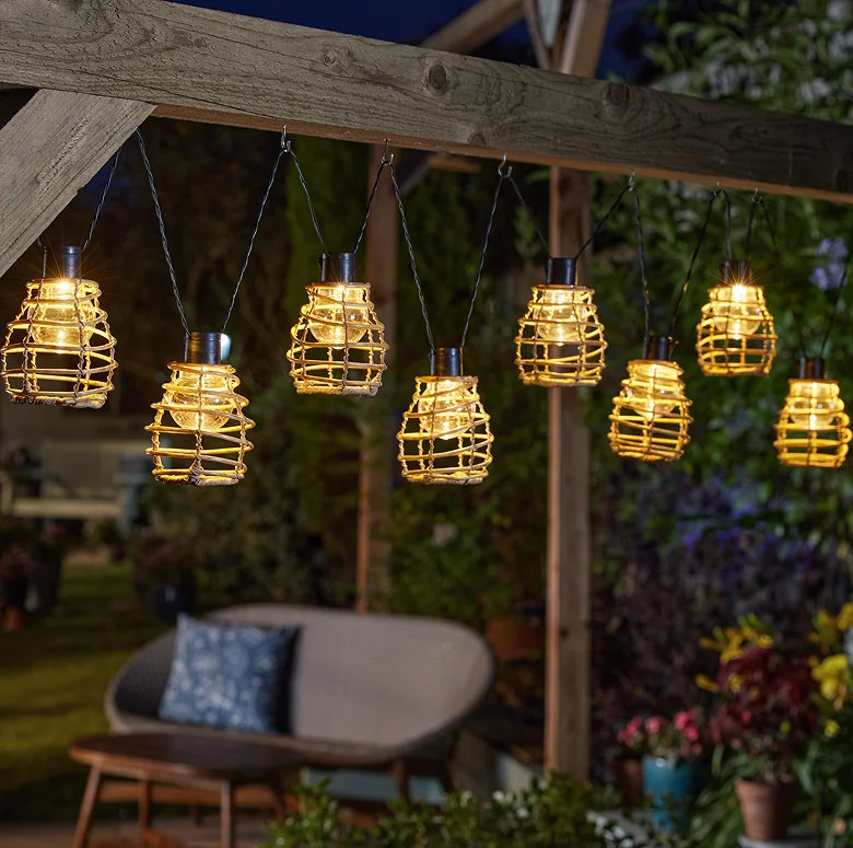 Woven lantern string lights hanging across a garden pergola at night