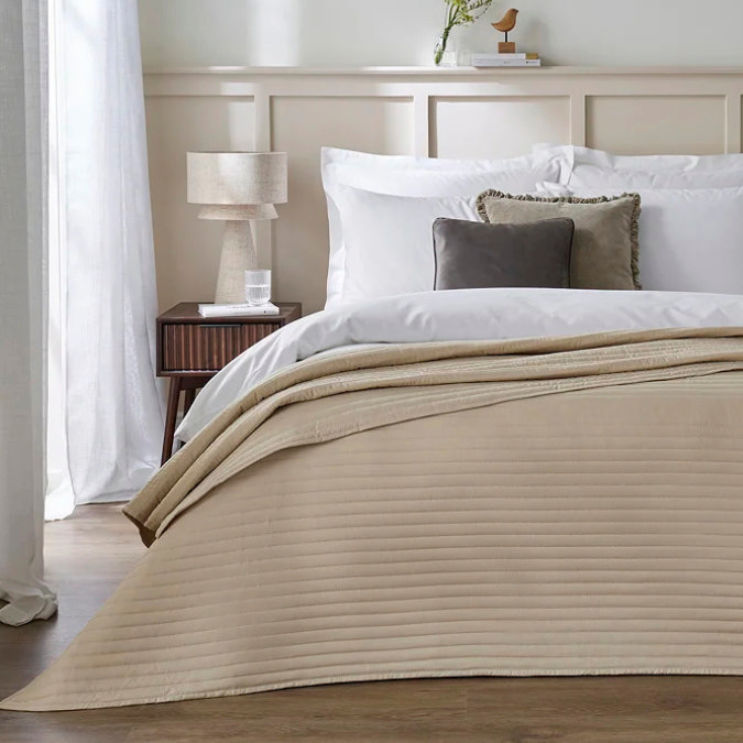 Neutral bedroom with beige quilted bedspread layered over white bedding and cushions