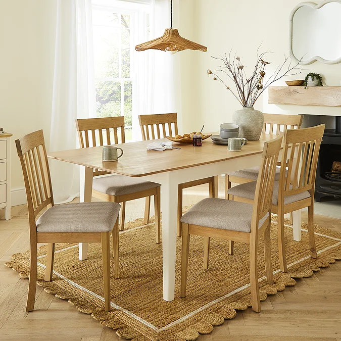 Slat-back oak dining chairs arranged around a two-tone farmhouse table, demonstrating balanced scale and comfortable chair spacing.