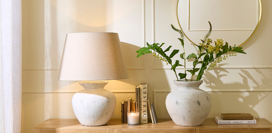 Faux green and yellow floral arrangement styled in a rustic white vase on a wooden console table, paired with a neutral lamp and candle for soft, welcoming hallway décor.