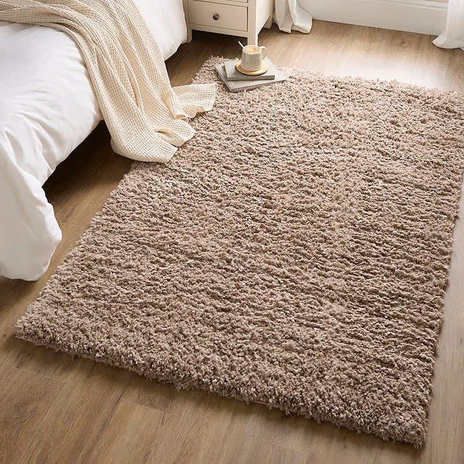 Warm taupe shaggy rug beside a bed in a cosy bedroom, showing a thick high-pile texture that adds softness, warmth and comfort underfoot for a home office or sleep space on wooden flooring