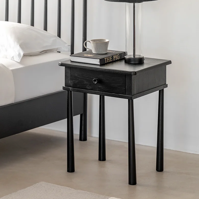 bedroom with black wooden bedside table featuring single drawer and slim legs