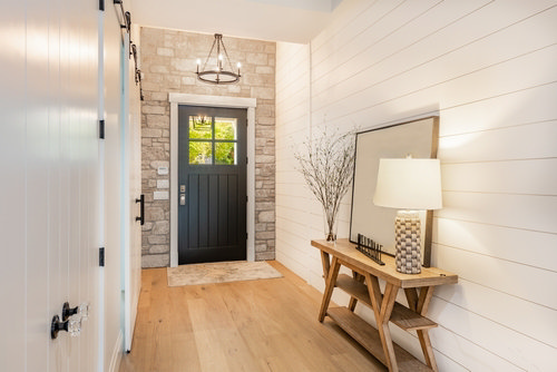 Light, bright hallway with white shiplap walls, light wood floor, glass-panel front door, slim console and mirror—ideas to make a narrow entry look wider.
