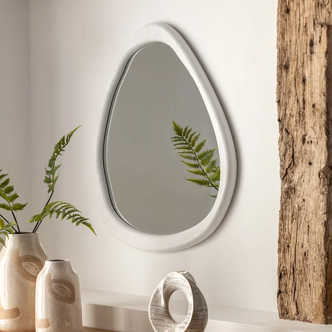 White pebble-shaped wall mirror with smooth curved frame, adding a modern organic touch to a living room wall.