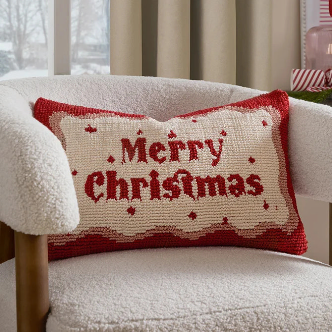 Red and cream Christmas cushion with Merry Christmas text on boucle armchair by festive window