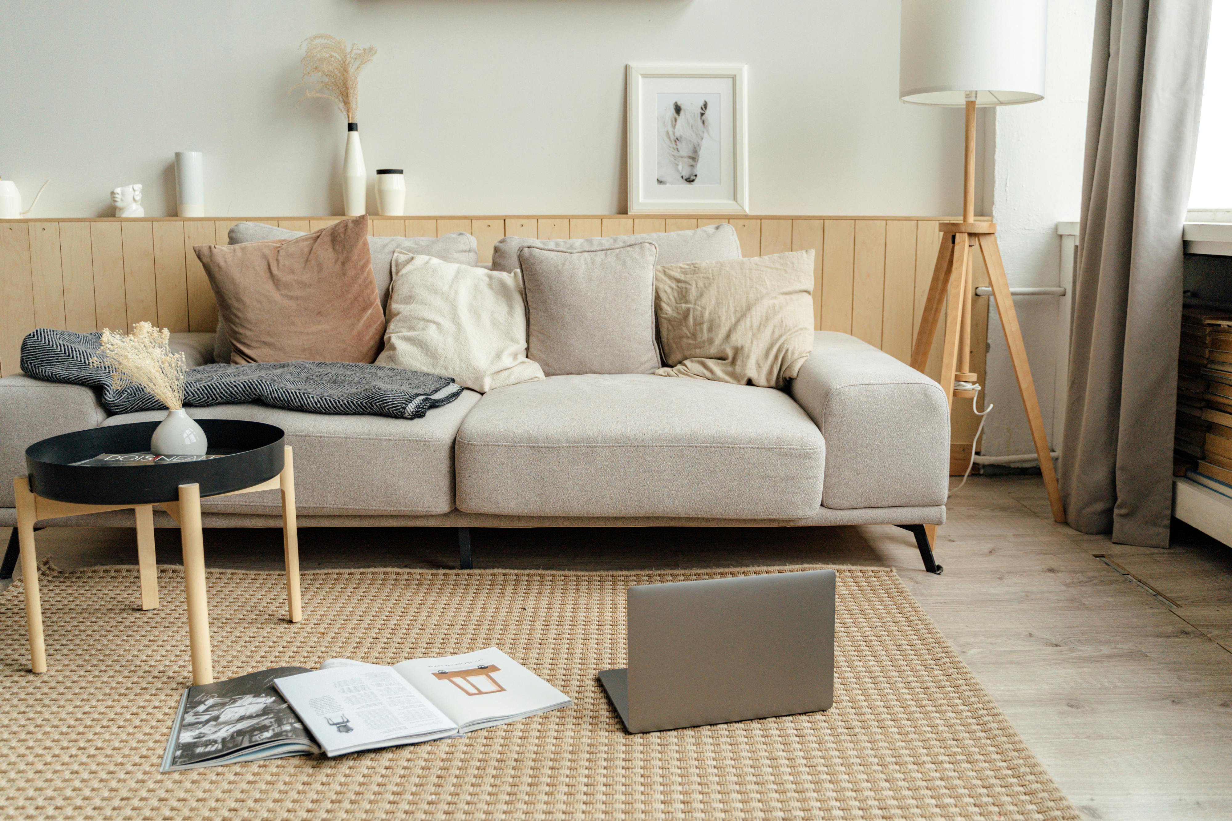 Neutral two‑seater sofa styled with five mixed‑size beige‑and‑tan cushions, a charcoal throw and a black‑tray coffee table on a jute rug