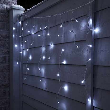 white icicle lights hanging on a fence, lit up at night