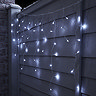 white icicle lights hanging on a fence, lit up at night