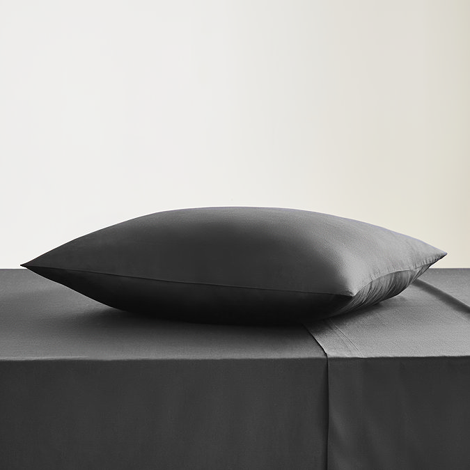 square coloured pillow in black cotton sateen pillowcase, resting on matching flat sheet on bed