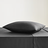 square coloured pillow in black cotton sateen pillowcase, resting on matching flat sheet on bed