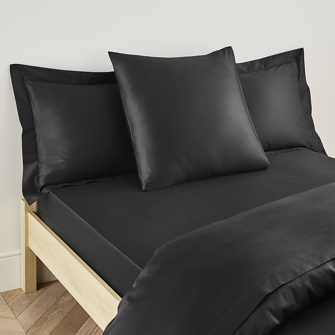 square pillow in black cotton sateen pillowcase, between two standard pillows, at the head of a bed