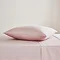 square coloured pillow in pale pink pillowcase, resting on matching flat sheet on bed