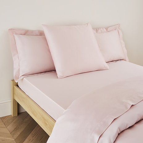 square pillow in blush pink cotton sateen pillowcase, between two standard pillows, at the head of a bed