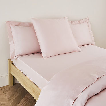 square coloured pillow in pale pink pillowcase, resting on matching flat sheet on bed