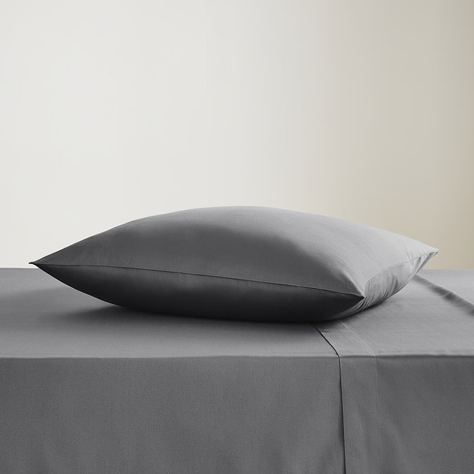 square coloured pillow in charcoal grey pillowcase, resting on matching flat sheet on bed