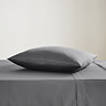 square coloured pillow in charcoal grey pillowcase, resting on matching flat sheet on bed