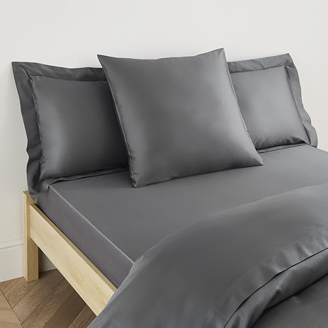 square pillow in charcoal grey cotton sateen pillowcase, between two standard pillows, at the head of a bed