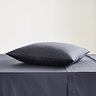 square coloured pillow in dark blue pillowcase, resting on matching flat sheet on bed