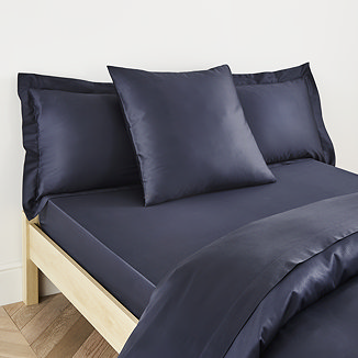 square pillow in dark blue cotton sateen pillowcase, between two standard pillows, at the head of a bed