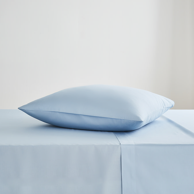 square coloured pillow in light blue pillowcase, resting on matching flat sheet on bed