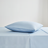 square coloured pillow in light blue pillowcase, resting on matching flat sheet on bed