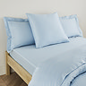 square pillow in light blue cotton sateen pillowcase, between two standard pillows, at the head of a bed