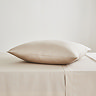 square coloured pillow in natural pillowcase, resting on matching flat sheet on bed
