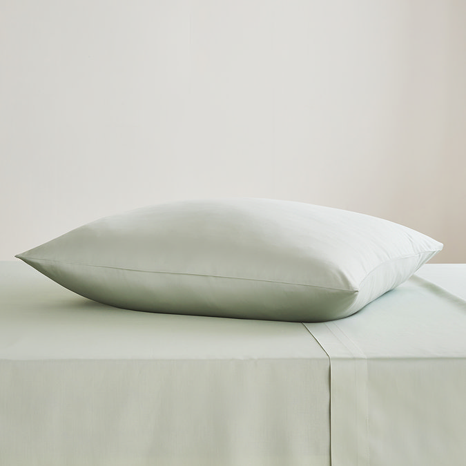 square coloured pillow in sage green pillowcase, resting on matching flat sheet on bed