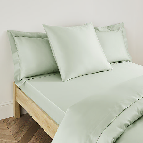 square pillow with sage green pillowcase in the middle of two standard pillows at the head of a bed