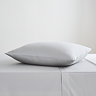 square coloured pillow in silver pillowcase, resting on matching flat sheet on bed