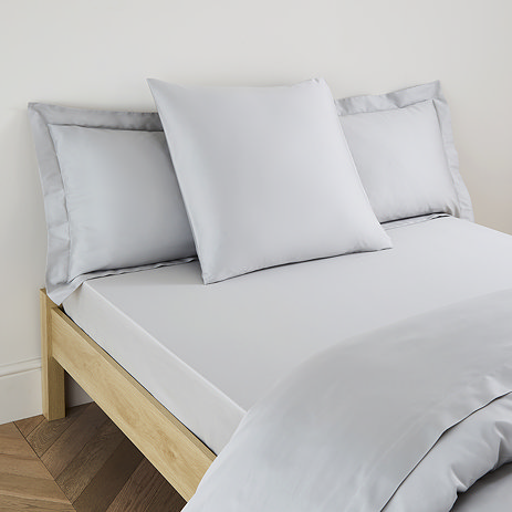 square pillow in silver cotton sateen pillowcase, between two standard pillows, at the head of a bed
