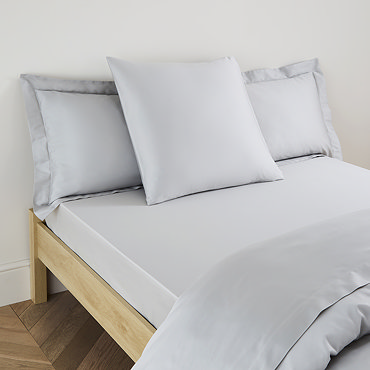 square coloured pillow in silver pillowcase, resting on matching flat sheet on bed