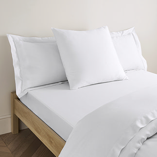 square pillow in white cotton sateen pillowcase, between two standard pillows, at the head of a bed