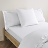 square pillow in white cotton sateen pillowcase, between two standard pillows, at the head of a bed