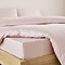 close-up on corner of bed with pale pink fitted sheet over the mattress, matching duvet set pulled back to reveal fit, and matching pillowcases