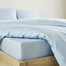 close-up on corner of bed with light blue fitted sheet over the mattress, matching duvet set pulled back to reveal fit, and matching pillowcases
