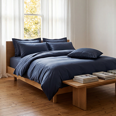 dark blue duvet cover folded with matching oxford and standard pillows stacked on top