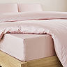 close-up on corner of bed with pale pink fitted sheet over the mattress, matching duvet set pulled back to reveal fit, and matching pillowcases