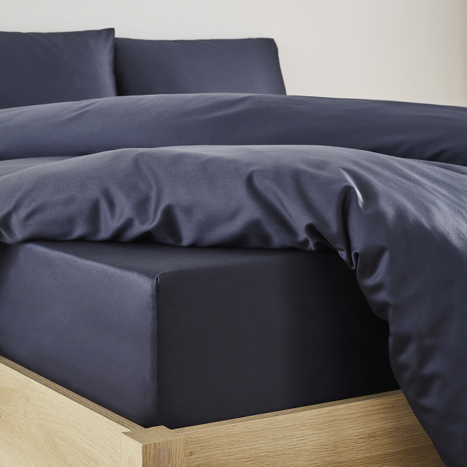 close-up on corner of bed with dark blue fitted sheet over the mattress, matching duvet set pulled back to reveal fit, and matching pillowcases